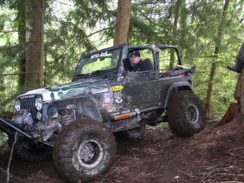 1979 Ford Bronco - A driver navigates a muddy, off-road path in a heavily modified Jeep Wrangler.