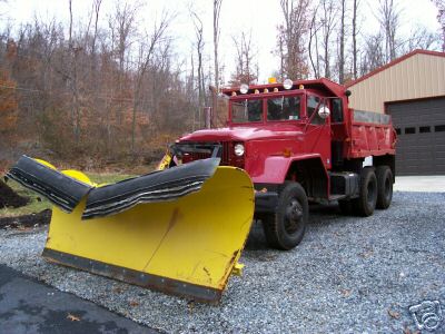 1968 Jeep CJ5 - A red dump truck equipped with a large yellow snow plow is parked on a gravel surface in front of a building.