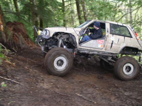 1979 Ford Bronco - A modified off-road vehicle navigates a challenging muddy trail through a wooded area.