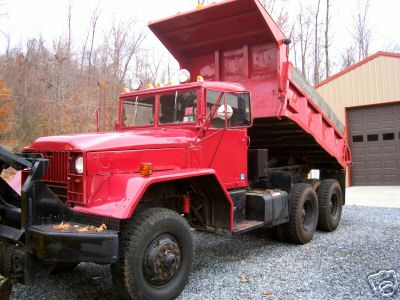 Red dump truck with a plow attachment parked in front of a garage