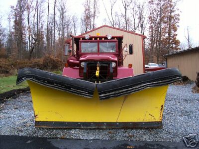 1968 Jeep CJ5 - A red truck is equipped with a large yellow snow plow, parked in front of a building.
