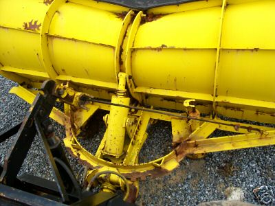 1968 Jeep CJ5 - A close-up view of a yellow snow plow attachment, showing its hydraulic system and signs of rust.