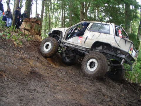 1979 Ford Bronco - Modified off-road vehicle tackles a challenging muddy hill climb in a wooded area.