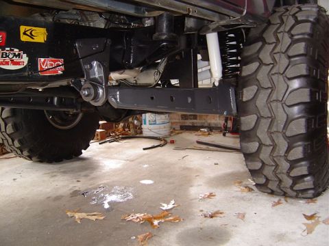 1986 Ford Bronco - Under-truck view of a lifted front suspension showing long black boxed extended radius arms, coil springs, a white-bodied shock, and large…