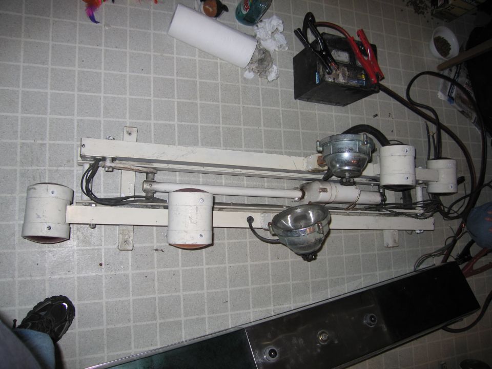 Fluorescent light fixture, car battery with jumper cables, and a chrome trim piece on a tiled floor
