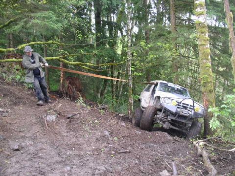 1979 Ford Bronco - A man pulls a white SUV out of a muddy ditch in a forest using a tow strap.