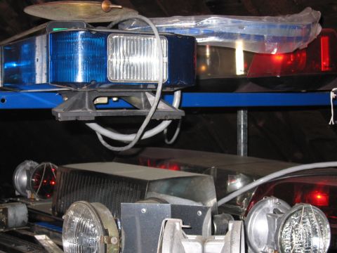 1991 Ford LTD Crown Victoria - Various emergency vehicle parts, including a light bar and headlights, are stored on shelves.