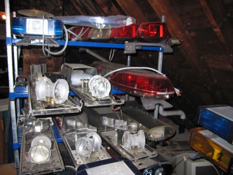 1991 Ford LTD Crown Victoria - Various police light bars and vehicle light parts are stored on shelves in an attic space.
