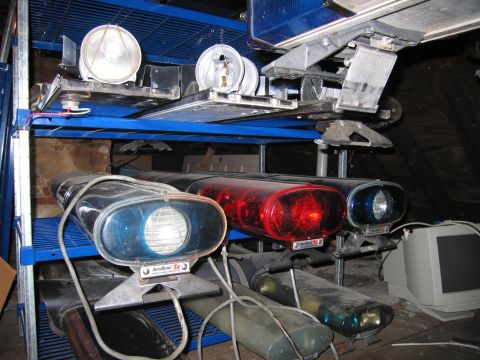 1991 Ford LTD Crown Victoria - Collection of police light bars and spotlights stored on shelving units, alongside a vintage computer monitor.