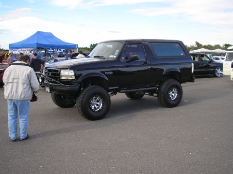 1995 Ford Bronco - Lifted black 1995 Ford Bronco on display at an outdoor event with other vehicles present.