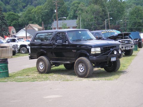 1995 Ford Bronco - A lifted black Ford Bronco is parked on grass with other vehicles in the background.