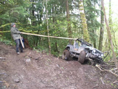 1979 Ford Bronco - Off-road vehicle stuck on a muddy incline in a wooded area, with people attempting to assist.