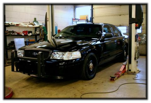 1998 Ford Crown Victoria - A black 2003 Ford Crown Victoria, equipped with a push bar, is raised on a car lift inside a workshop.