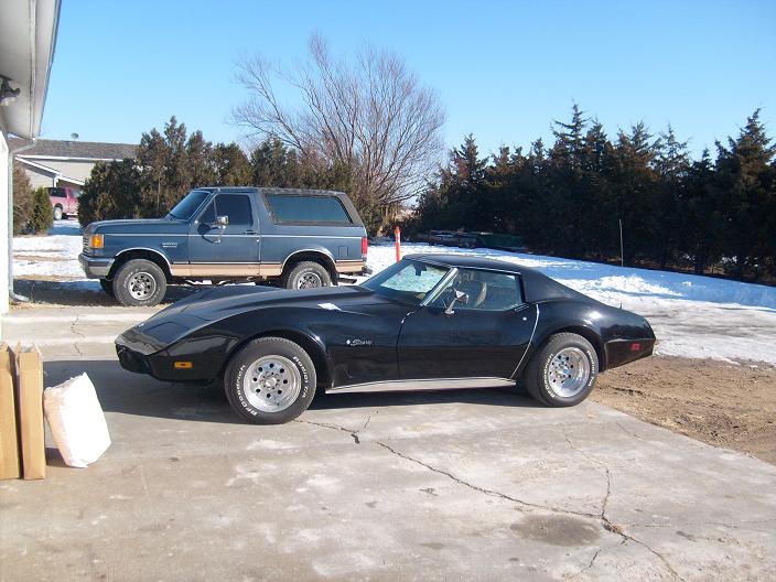 Black 1975 Chevrolet Corvette parked next to a blue Ford Bronco in a driveway