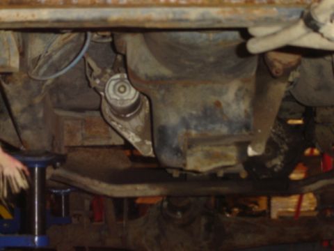 1992 Ford Bronco - The underside of a vehicle is viewed from below, revealing mechanical components and rust.