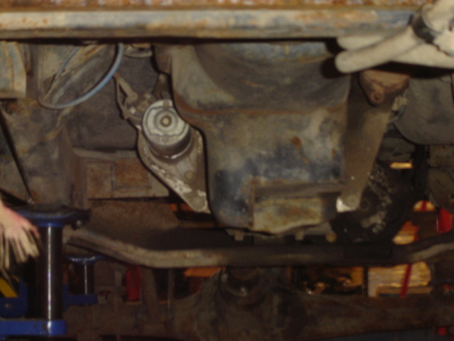 Underside of a rusty vehicle, showing engine components and suspension parts