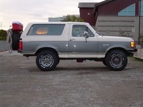 1991 Ford Bronco - This two-tone Ford Bronco is viewed from the side, showing its spare tire and a red cooler on the back.