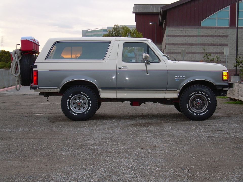 Two-tone grey and white Ford Bronco with a spare tire and red cooler mounted on the rear