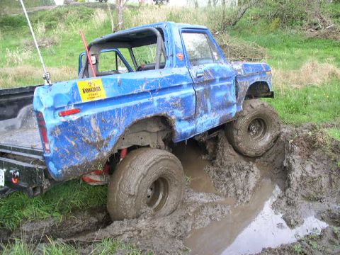 1979 Ford Bronco - This blue pickup truck is deeply stuck in thick mud, with its tires submerged.