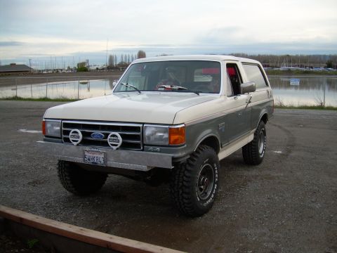 1991 Ford Bronco - This two-tone Ford Bronco is parked near a body of water under an overcast sky.