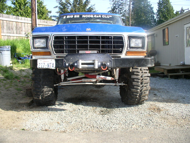 Lifted blue and white Ford Bronco on mud tires with winch bumper, front view on gravel