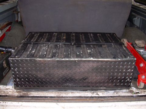 1991 Ford Bronco - A diamond plate toolbox is stored in the bed of a truck, next to a red jack.