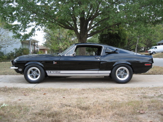 1968 Shelby GT500 - Side view of a black 1968 Shelby GT500 with silver racing stripes and aftermarket wheels.