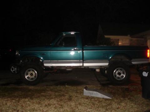 1996 Ford F-150 - A teal Ford F-150 pickup truck is parked outside at night, showing its lifted suspension and large wheels.