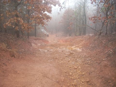 1992 Ford Bronco - A white SUV navigates a wet, muddy, and rocky path through a misty forest.