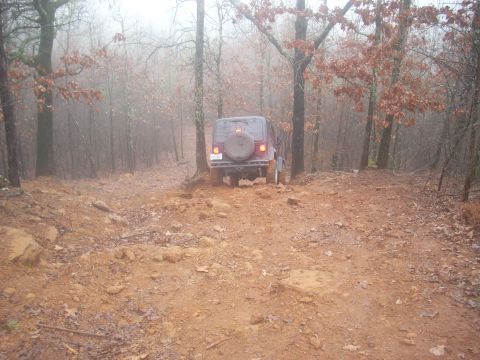 1992 Ford Bronco - Jeep Wrangler TJ navigates a challenging muddy path through a wooded area.