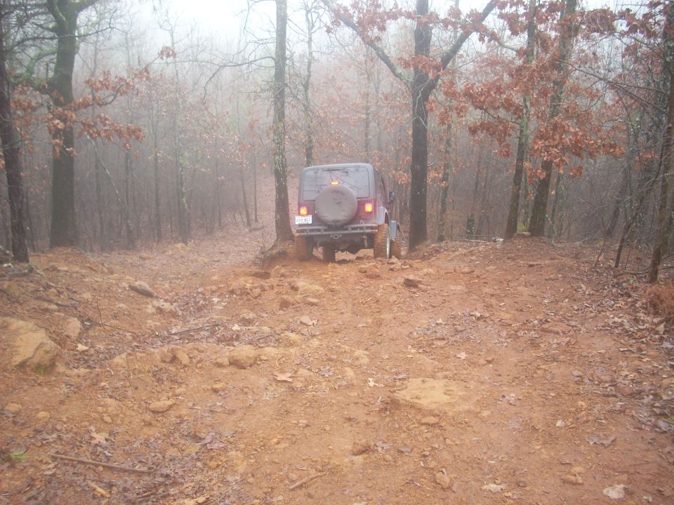 Jeep Wrangler TJ driving on a muddy forest trail