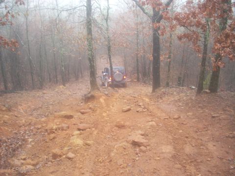 1992 Ford Bronco - A Jeep Wrangler navigates a challenging off-road trail in a misty forest.