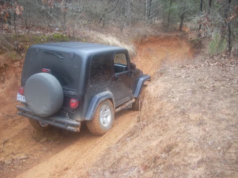 1992 Ford Bronco - Jeep Wrangler navigating a challenging muddy trail through a wooded area.
