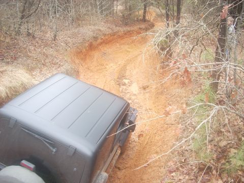 1992 Ford Bronco - A Jeep navigates a challenging muddy off-road path surrounded by trees.