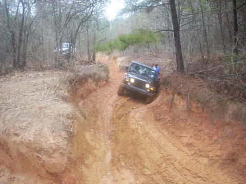 1992 Ford Bronco - A Jeep Wrangler navigates a challenging muddy off-road trail, with another vehicle in the distance.