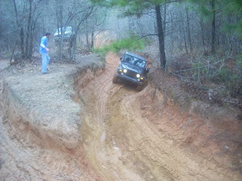 1992 Ford Bronco - A Jeep Wrangler navigates a challenging muddy off-road course with another vehicle visible in the background.