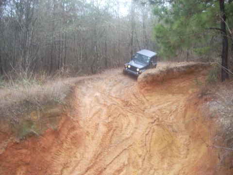 1992 Ford Bronco - A Jeep navigates a challenging muddy off-road trail with steep inclines and deep ruts.