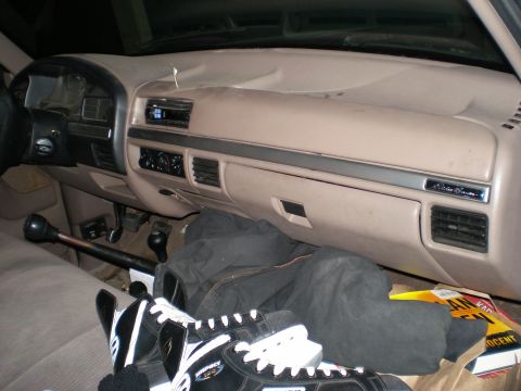 1995 Ford F-150 - The interior of a 1995 Ford F-150 shows a tan dashboard, floor mats, and a gear shift lever.