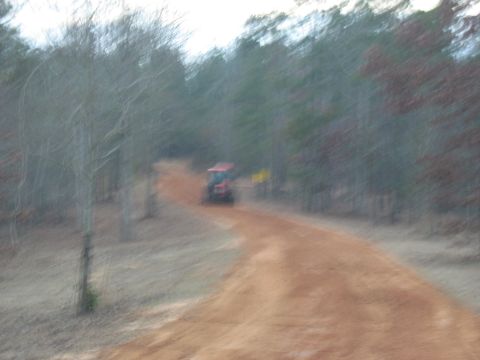 1978 Ford Bronco - A red tractor is seen from behind on a dirt road in a forest.