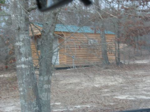 1978 Ford Bronco - A small log cabin sits in a clearing, partially obscured by trees.