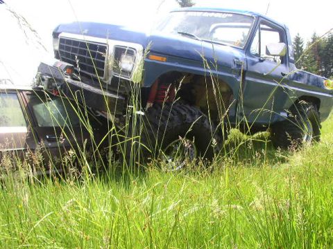1979 Ford Bronco - A blue pickup truck with a heavily damaged front end is parked in tall grass, with another vehicle visible behind it.