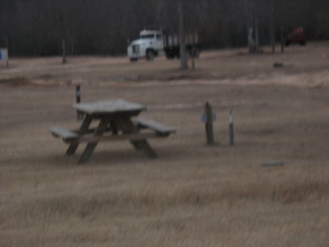 1978 Ford Bronco - A white dump truck is visible in the background of a rural scene, with a picnic table in the foreground.