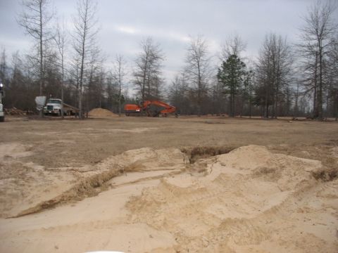 1978 Ford Bronco - An orange excavator and a white truck are visible at a construction site with piles of sand and bare trees.