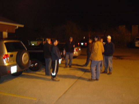 1986 Ford Bronco - People stand around vehicles in a parking lot after dark.