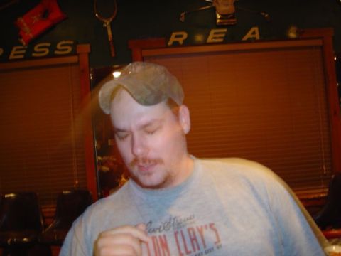 1986 Ford Bronco - A man wearing a baseball cap and a t-shirt with text is the focus of this indoor photograph.