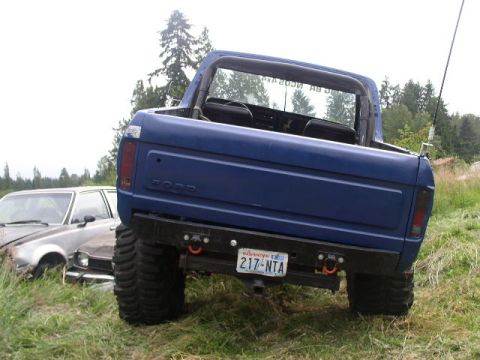 1979 Ford Bronco - A blue Ford Bronco is parked next to a damaged car in a field.