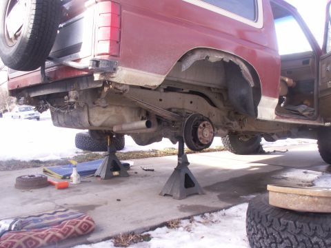 1986 Ford Bronco - This red SUV is undergoing repairs with its rear axle disassembled and supported by jack stands.