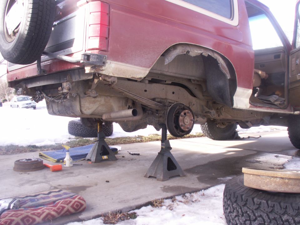 Red SUV on jack stands, rear axle removed, spare tire mounted on tailgate