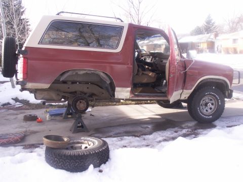1986 Ford Bronco - This red and white SUV is up on jack stands with its rear wheels removed, suggesting maintenance work is underway.