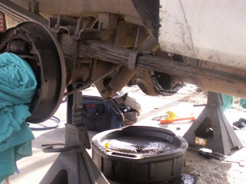 1986 Ford Bronco - A vehicle's rear axle and suspension components are visible while undergoing maintenance, with tools and an oil pan nearby.